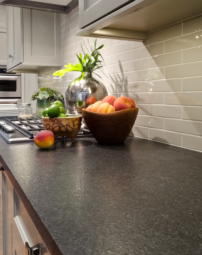 Klassisk inredning av ett mellanstort kök, med en undermonterad diskho, luckor med infälld panel, grå skåp, granitbänkskiva, grått stänkskydd, stänkskydd i glaskakel, rostfria vitvaror, mellanmörkt trägolv och en köksö