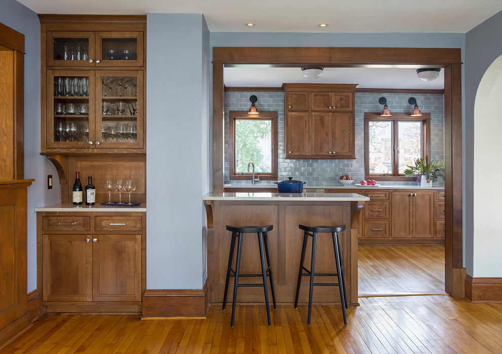Foto på ett mellanstort amerikanskt kök, med en undermonterad diskho, släta luckor, skåp i mellenmörkt trä, bänkskiva i kvarts, blått stänkskydd, stänkskydd i keramik, rostfria vitvaror, ljust trägolv och brunt golv