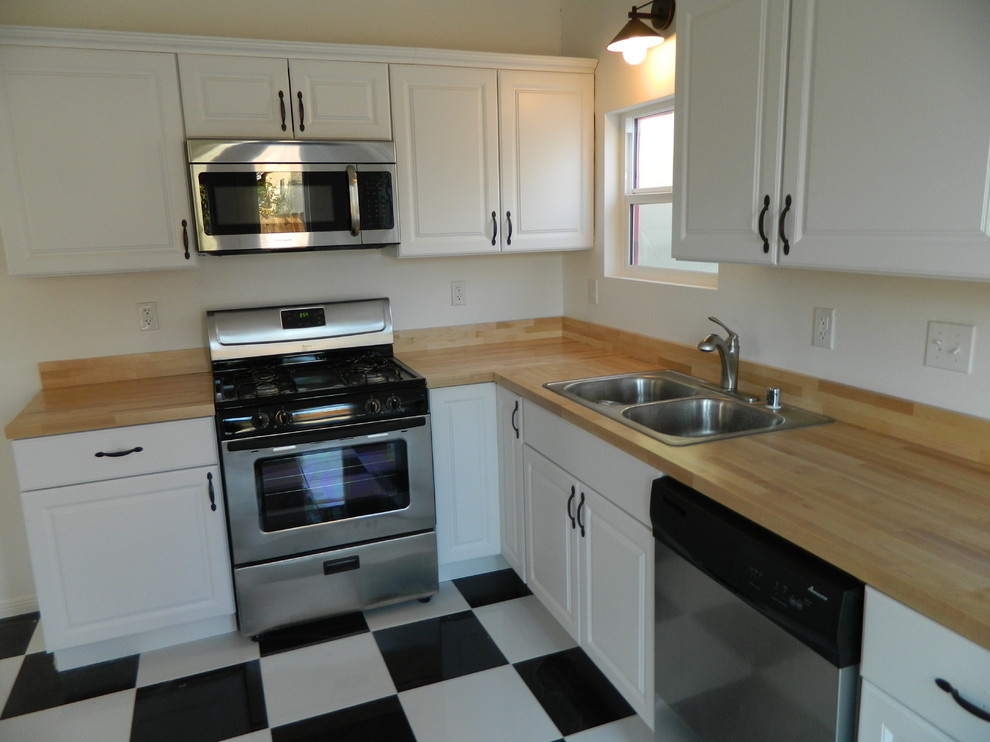 This is an example of a small classic l-shaped kitchen/diner in Los Angeles with a double-bowl sink, shaker cabinets, white cabinets, wood worktops, stainless steel appliances, ceramic flooring, white splashback, no island, multi-coloured floors and brown worktops.