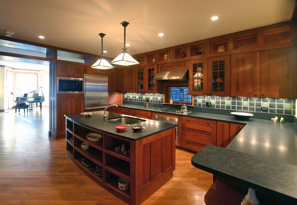Bild på ett vintage kök, med en undermonterad diskho, skåp i shakerstil, skåp i mörkt trä, grått stänkskydd, stänkskydd i cementkakel, rostfria vitvaror, mellanmörkt trägolv, en köksö och bänkskiva i täljsten