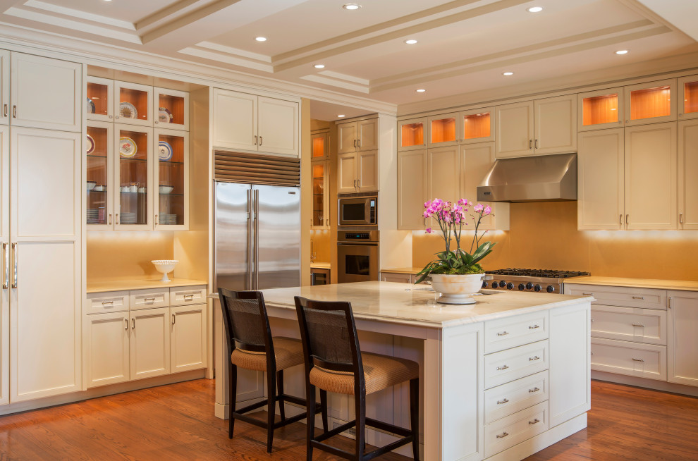 Mid-sized transitional l-shaped medium tone wood floor, brown floor and coffered ceiling eat-in kitchen photo in Chicago with an undermount sink, recessed-panel cabinets, white cabinets, quartz countertops, beige backsplash, quartz backsplash, stainless steel appliances, an island and beige countertops