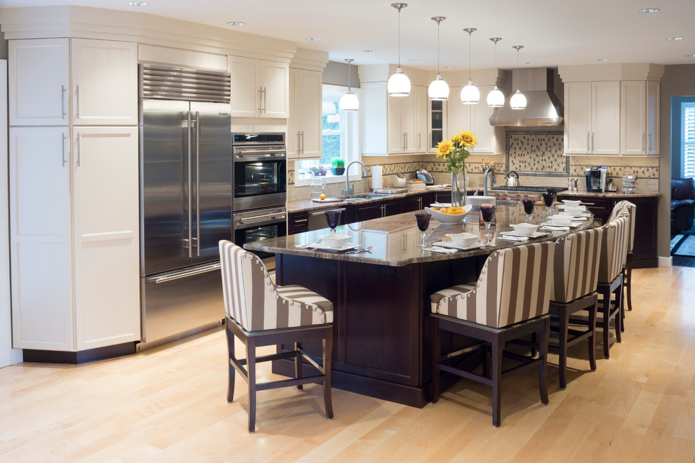 Huge elegant l-shaped light wood floor open concept kitchen photo in Providence with stainless steel appliances, granite countertops, an island, shaker cabinets, white cabinets, beige backsplash, stone tile backsplash and an undermount sink