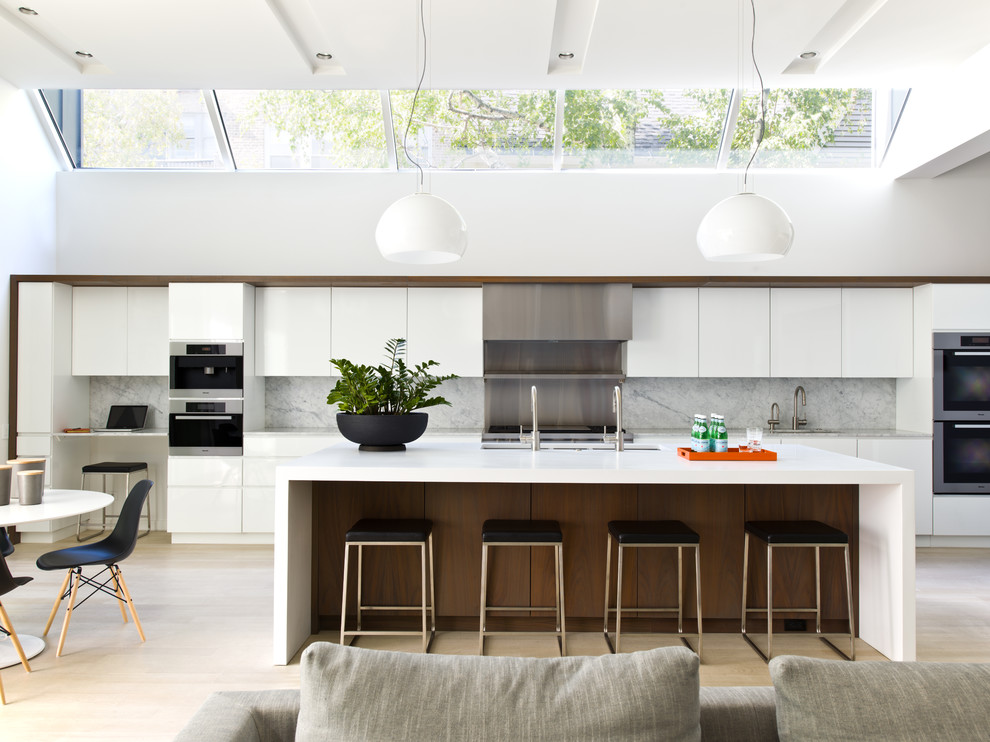 Bild på ett mellanstort funkis kök, med släta luckor, vita skåp, marmorbänkskiva, vitt stänkskydd, stänkskydd i sten, rostfria vitvaror, ljust trägolv och en köksö