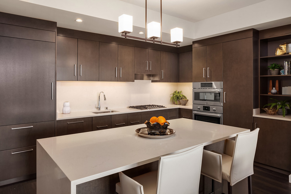 Example of a trendy l-shaped dark wood floor kitchen design in Seattle with an undermount sink, flat-panel cabinets, dark wood cabinets, white backsplash, stainless steel appliances, an island and white countertops