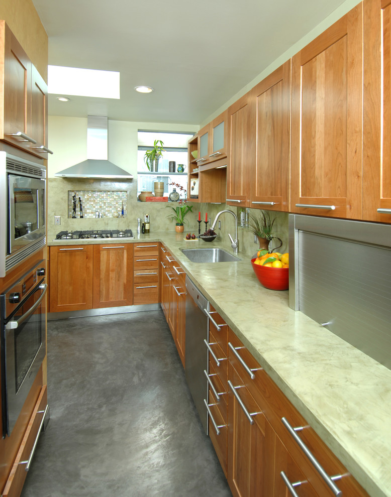 Asiatisk inredning av ett mellanstort kök, med en nedsänkt diskho, luckor med infälld panel, skåp i mellenmörkt trä, bänkskiva i betong, grönt stänkskydd, rostfria vitvaror och betonggolv