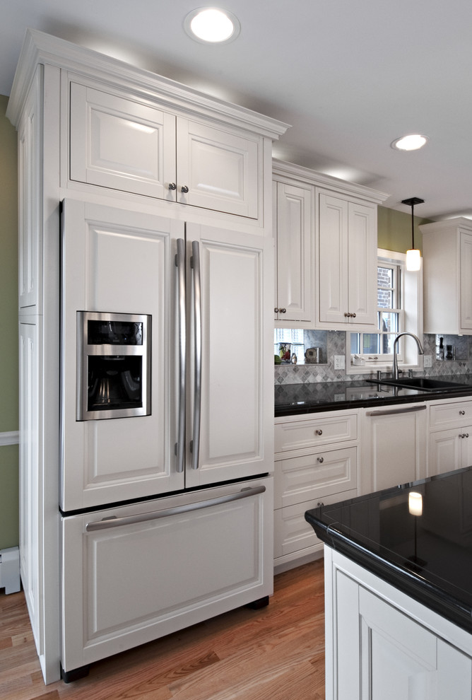 Example of a mid-sized trendy galley light wood floor enclosed kitchen design in Chicago with a drop-in sink, raised-panel cabinets, white cabinets, tile countertops, gray backsplash, ceramic backsplash, paneled appliances and an island