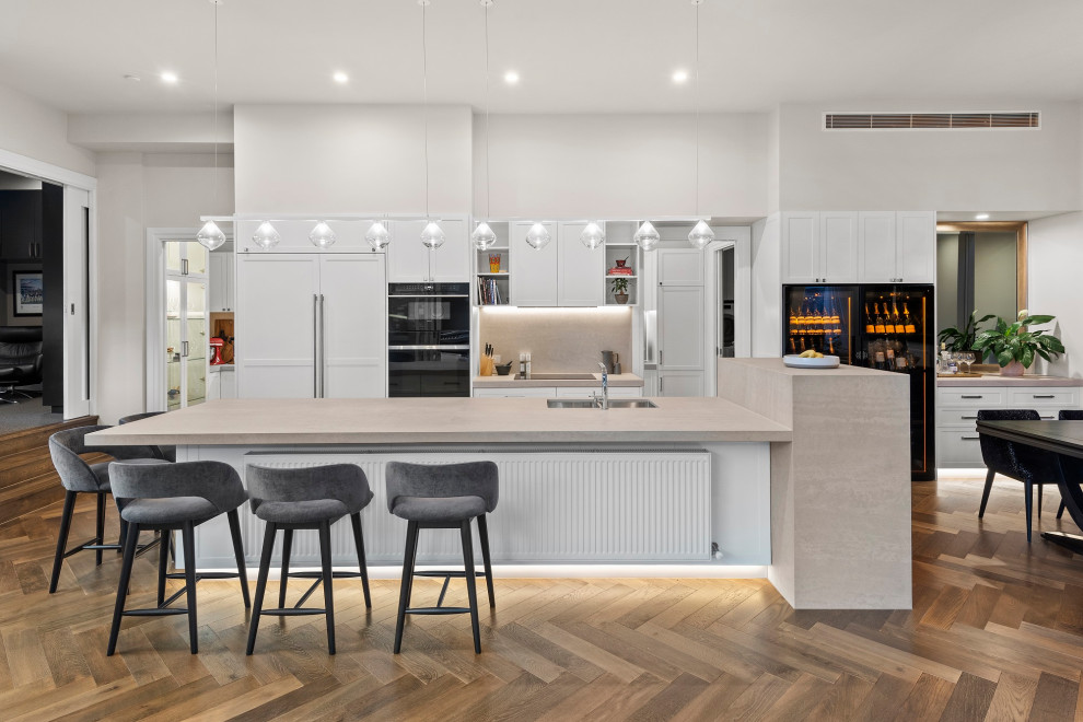 Inspiration for a large contemporary galley medium tone wood floor and brown floor open concept kitchen remodel in Melbourne with an undermount sink, recessed-panel cabinets, white cabinets, gray backsplash, paneled appliances, an island, beige countertops, granite countertops and granite backsplash