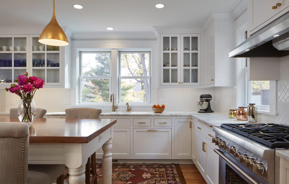 Diseño de cocina actual grande con fregadero bajoencimera, armarios estilo shaker, puertas de armario blancas, encimera de mármol, salpicadero blanco, salpicadero de azulejos de porcelana, electrodomésticos de acero inoxidable, suelo de madera clara y una isla