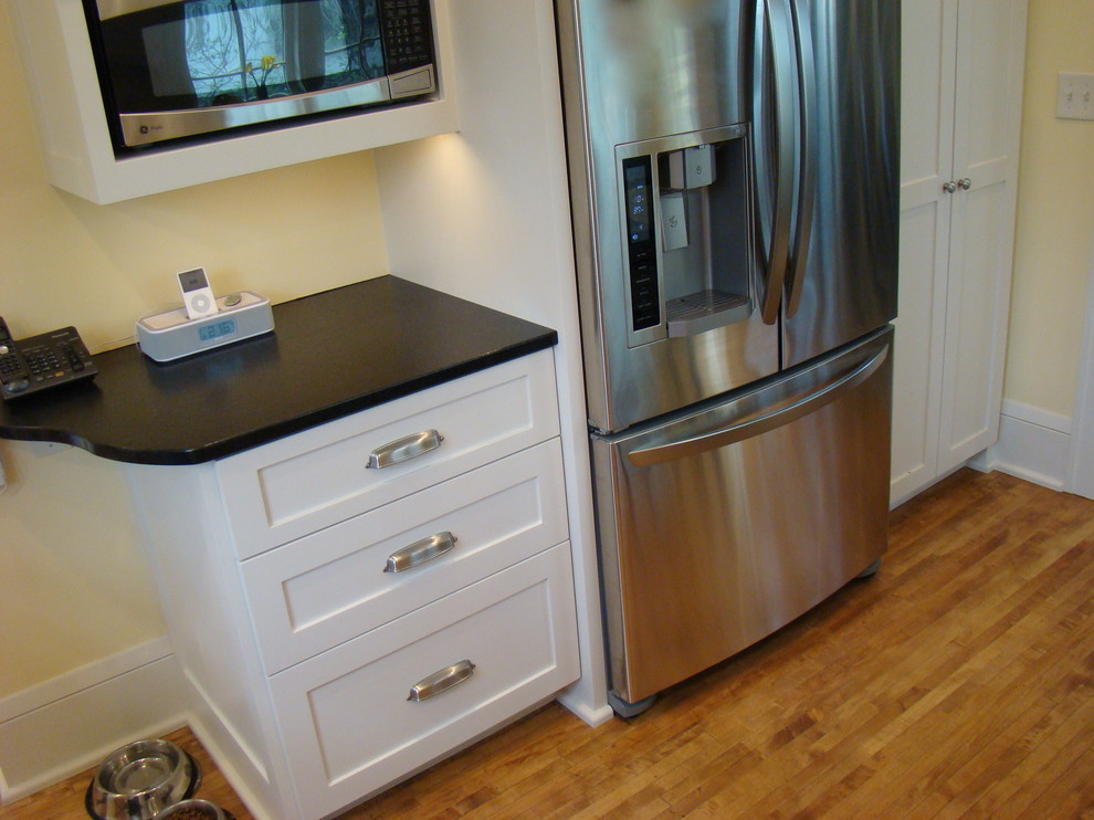 Medium sized traditional u-shaped enclosed kitchen in Minneapolis with a submerged sink, flat-panel cabinets, white cabinets, granite worktops, white splashback, ceramic splashback, stainless steel appliances, light hardwood flooring and a breakfast bar.