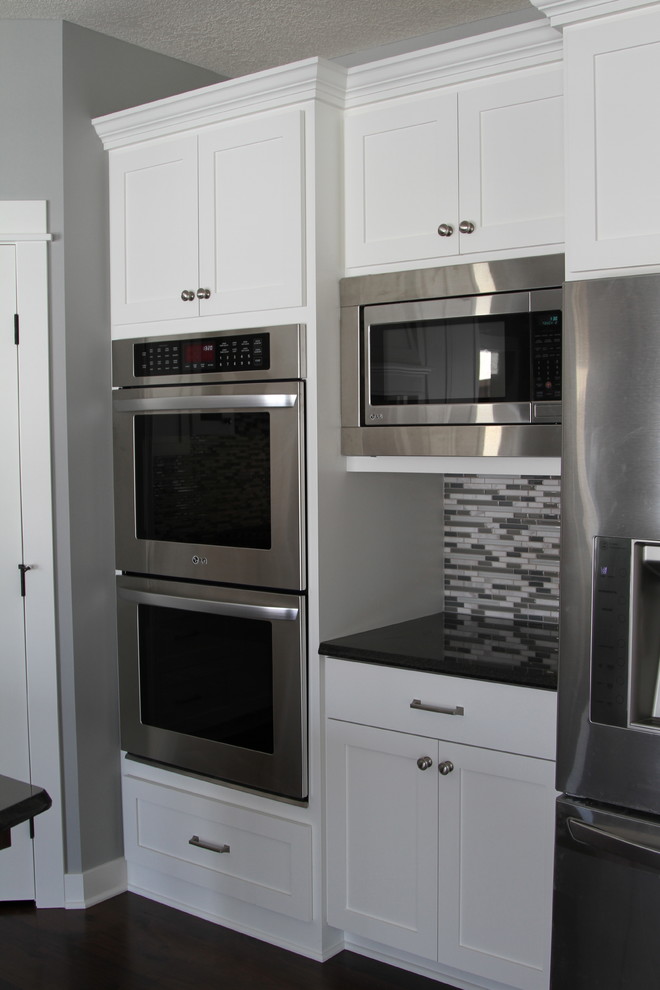 Example of an eat-in kitchen design in Minneapolis with an undermount sink, flat-panel cabinets, white cabinets, granite countertops, glass sheet backsplash and stainless steel appliances