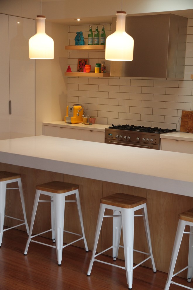 Mid-sized trendy l-shaped medium tone wood floor eat-in kitchen photo in Melbourne with an island, flat-panel cabinets, white cabinets, quartz countertops, white backsplash, subway tile backsplash and stainless steel appliances
