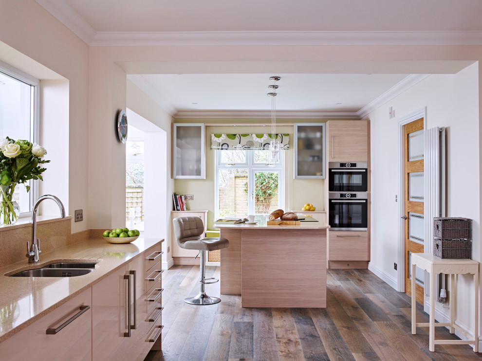 Design ideas for a classic l-shaped open plan kitchen in Surrey with a submerged sink, flat-panel cabinets, quartz worktops, black appliances, an island, light wood cabinets, dark hardwood flooring and brown floors.