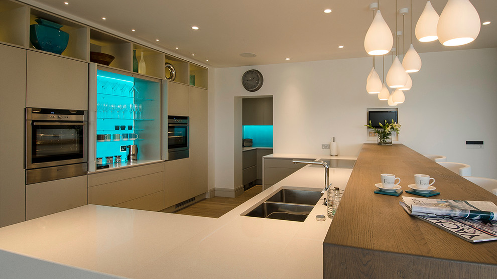 Medium sized modern u-shaped open plan kitchen in Cornwall with a double-bowl sink, flat-panel cabinets, grey cabinets, glass sheet splashback, stainless steel appliances and engineered stone countertops.