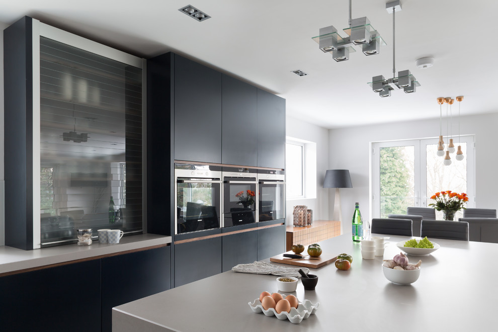 This is an example of a medium sized contemporary l-shaped kitchen/diner in London with flat-panel cabinets, blue cabinets, quartz worktops, white splashback, glass sheet splashback, integrated appliances, porcelain flooring and an island.