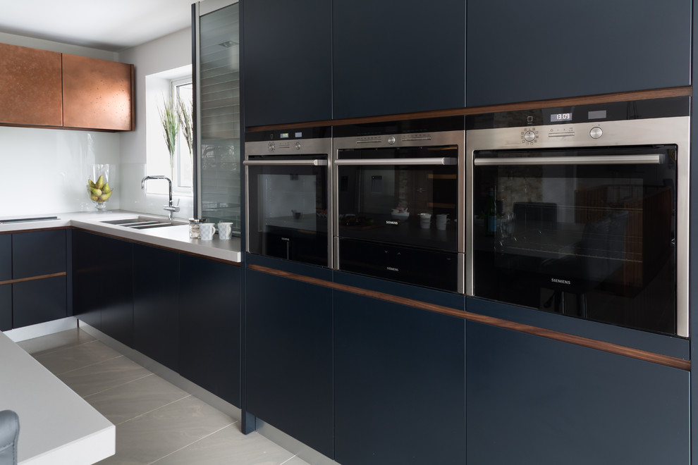 Design ideas for a medium sized contemporary l-shaped kitchen/diner in London with an integrated sink, flat-panel cabinets, blue cabinets, quartz worktops, white splashback, glass sheet splashback, integrated appliances, porcelain flooring and an island.