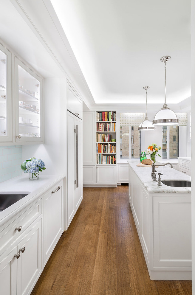 Klassisk inredning av ett stort vit vitt u-kök, med en undermonterad diskho, skåp i shakerstil, vita skåp, bänkskiva i kvarts, integrerade vitvaror, mellanmörkt trägolv, en köksö och brunt golv