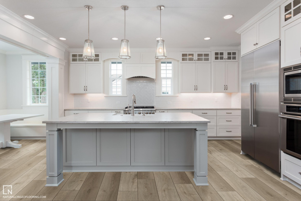 Foto på ett stort grå kök med öppen planlösning, med luckor med infälld panel, vita skåp, vitt stänkskydd, stänkskydd i tunnelbanekakel, rostfria vitvaror, vinylgolv, en köksö och beiget golv