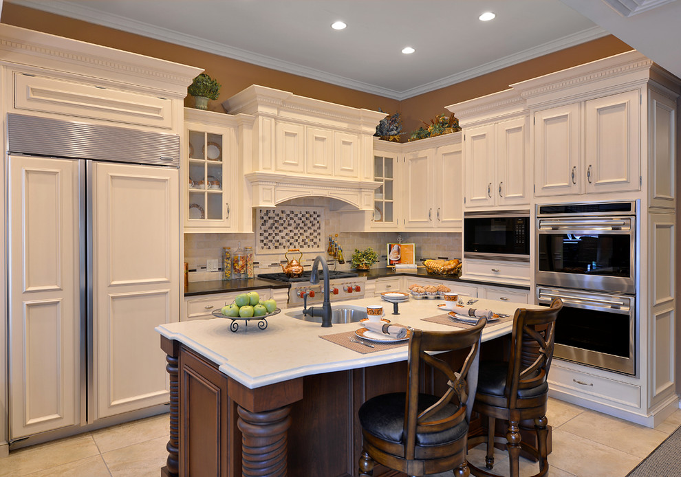 Klassisk inredning av ett kök, med en undermonterad diskho, luckor med infälld panel, vita skåp, bänkskiva i kvarts, integrerade vitvaror och en köksö