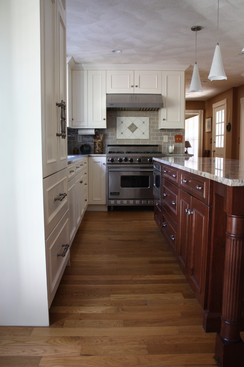 Transitional kitchen with white perimeter cabinets and dark island in polyurethane (PU) finish, featuring granite countertop and hardwood floors