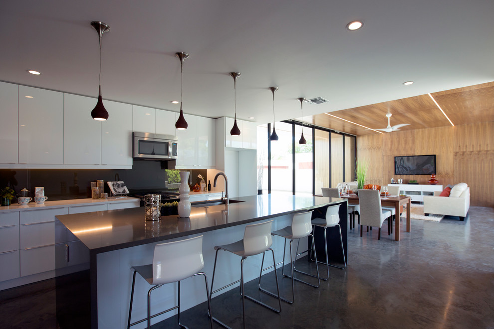 Example of a large trendy concrete floor open concept kitchen design in Phoenix with a single-bowl sink, flat-panel cabinets, white cabinets, quartz countertops, gray backsplash, glass sheet backsplash, stainless steel appliances and an island