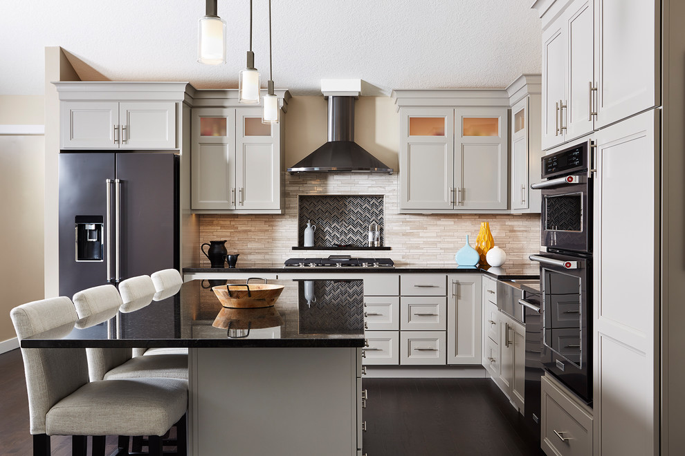 Klassische Küche in L-Form mit Landhausspüle, Schrankfronten mit vertiefter Füllung, Küchenrückwand in Beige, Rückwand aus Stäbchenfliesen, dunklem Holzboden, Kücheninsel und grauen Schränken