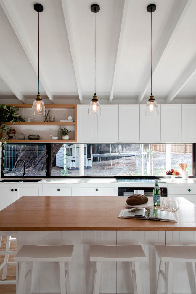 Inspiration för ett mellanstort funkis vit vitt kök, med en undermonterad diskho, skåp i shakerstil, vita skåp, bänkskiva i kvarts, fönster som stänkskydd, vita vitvaror, mellanmörkt trägolv, en köksö och brunt golv