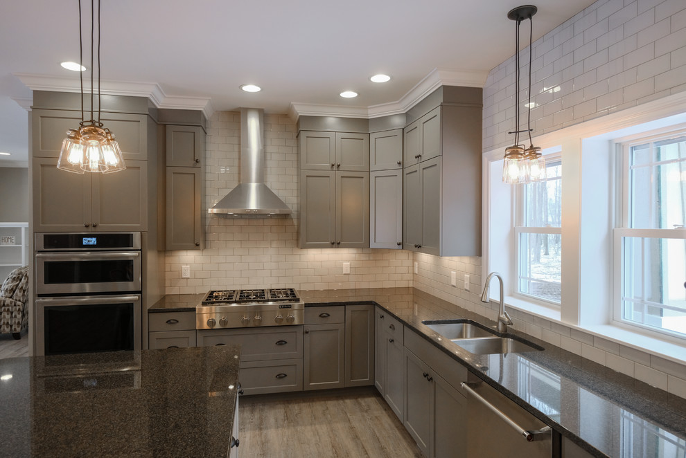 Example of a large urban u-shaped medium tone wood floor and brown floor eat-in kitchen design in Other with an undermount sink, gray cabinets, granite countertops, white backsplash, stainless steel appliances, an island, shaker cabinets and subway tile backsplash