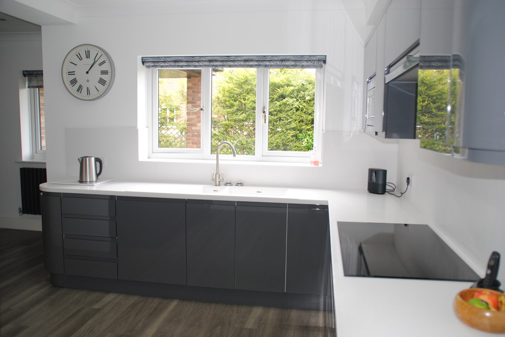 Photo of a large modern kitchen/diner in Other with an integrated sink, flat-panel cabinets, grey cabinets, composite countertops, white splashback, black appliances, a breakfast bar, grey floors and white worktops.