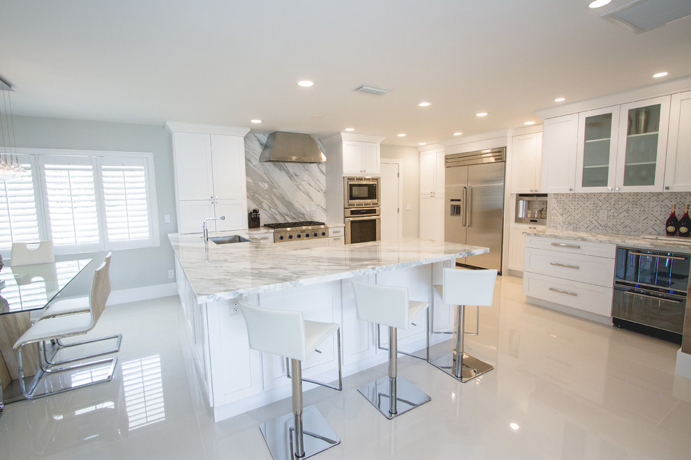Large trendy l-shaped porcelain tile and beige floor enclosed kitchen photo in Miami with an undermount sink, shaker cabinets, white cabinets, marble countertops, red backsplash, marble backsplash, stainless steel appliances, a peninsula and white countertops