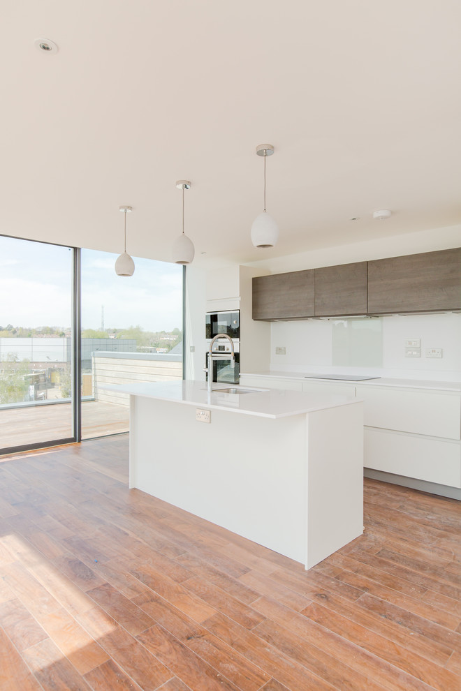 Inspiration for a medium sized industrial l-shaped open plan kitchen in Sussex with a built-in sink, flat-panel cabinets, white cabinets, engineered stone countertops, glass sheet splashback, integrated appliances, medium hardwood flooring and an island.