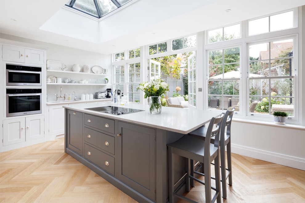 Einzeilige Klassische Küche mit Schrankfronten im Shaker-Stil, grauen Schränken, schwarzen Elektrogeräten, hellem Holzboden, Kücheninsel und beigem Boden in Sussex
