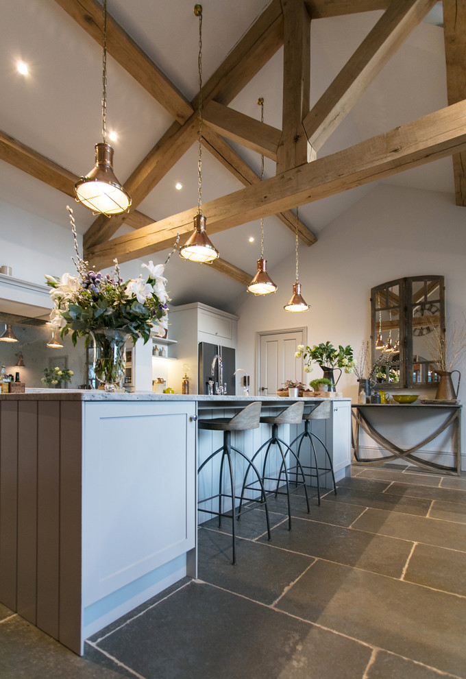 Inspiration for a large farmhouse single-wall kitchen/diner in Surrey with a belfast sink, shaker cabinets, grey cabinets, granite worktops, grey splashback, mirror splashback, stainless steel appliances, limestone flooring, an island, grey floors and white worktops.