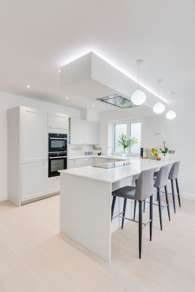 Inspiration for a contemporary u-shaped light wood floor and beige floor kitchen remodel in London with shaker cabinets, white cabinets, white backsplash, stainless steel appliances, a peninsula and white countertops
