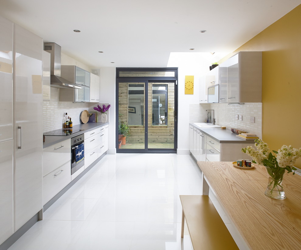 Inspiration for a contemporary galley kitchen in Other with flat-panel cabinets, white cabinets, yellow splashback, metro tiled splashback, stainless steel appliances and white floors.