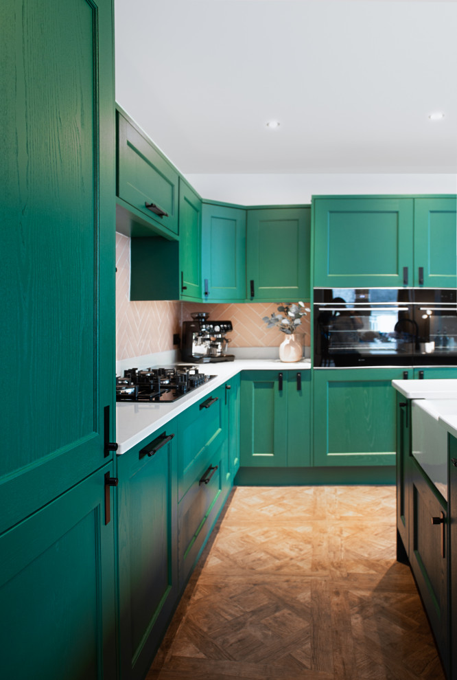 Foto på ett mellanstort funkis vit kök, med en rustik diskho, skåp i shakerstil, gröna skåp, granitbänkskiva, rosa stänkskydd, stänkskydd i keramik, svarta vitvaror, mörkt trägolv, en köksö och brunt golv