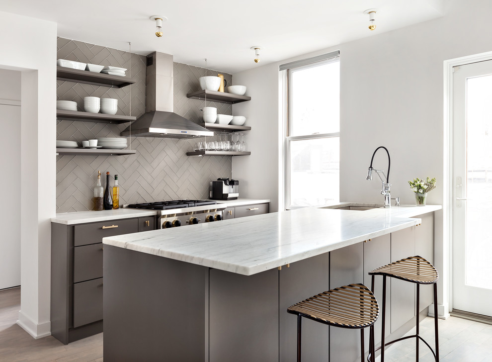 Small contemporary grey and white galley open plan kitchen in New York with a submerged sink, flat-panel cabinets, grey cabinets, grey splashback, metro tiled splashback, stainless steel appliances, light hardwood flooring and a breakfast bar.