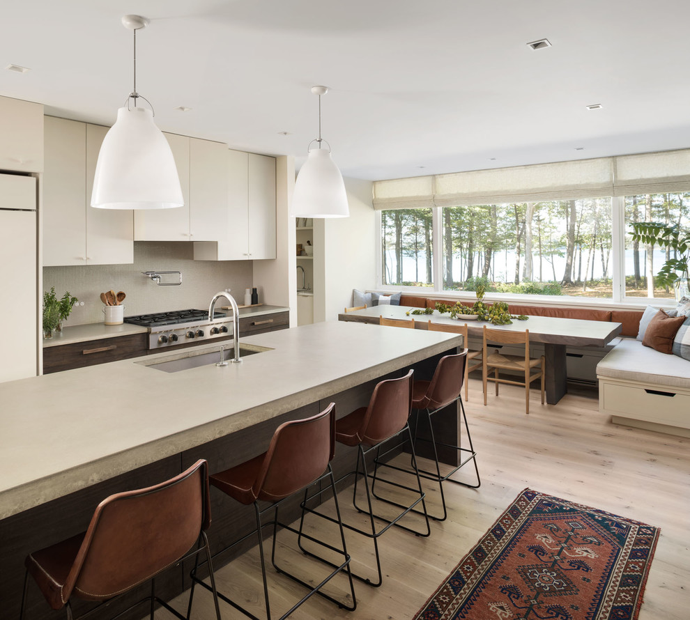 Contemporary kitchen/diner in Portland Maine with a submerged sink, flat-panel cabinets, beige cabinets, beige splashback, stainless steel appliances, light hardwood flooring, an island, beige floors and concrete worktops.