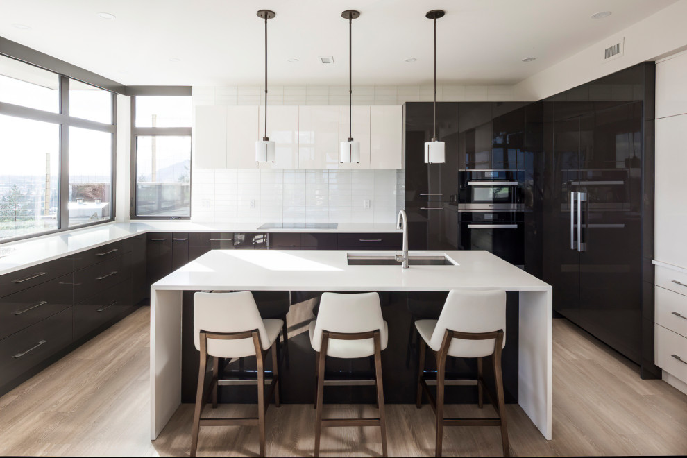 Photo of a contemporary u-shaped kitchen in Vancouver with a submerged sink, flat-panel cabinets, grey cabinets, white splashback, metro tiled splashback, integrated appliances, medium hardwood flooring, an island, brown floors and white worktops.