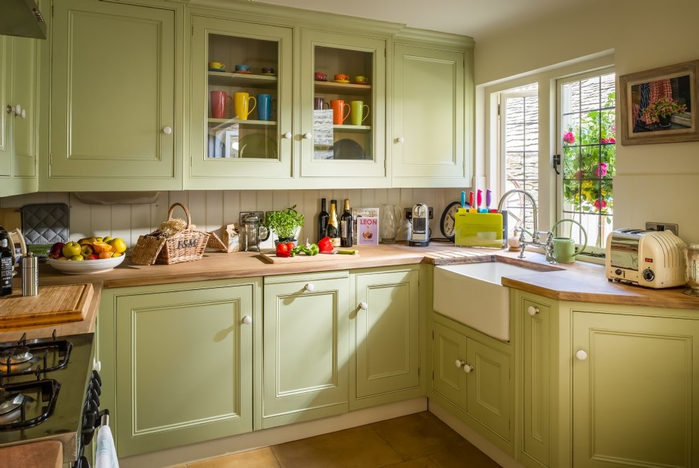 Example of a mid-sized farmhouse u-shaped ceramic tile and beige floor open concept kitchen design in Oxfordshire with a farmhouse sink, recessed-panel cabinets, green cabinets, wood countertops, white backsplash, wood backsplash, stainless steel appliances and no island