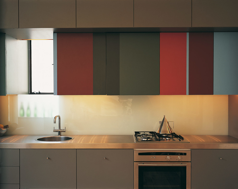 Bild på ett mellanstort kök, med släta luckor, röda skåp och bänkskiva i rostfritt stål