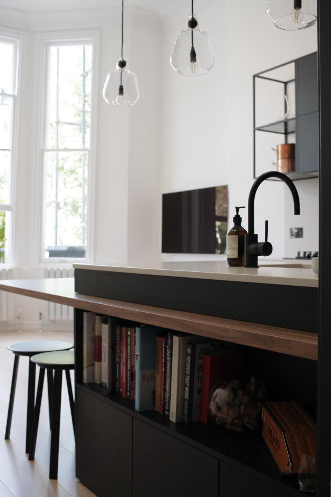 This is an example of a small contemporary galley open plan kitchen in London with flat-panel cabinets, black cabinets, quartz worktops, white splashback, an island and white worktops.