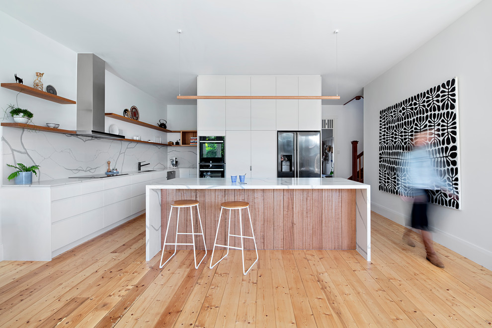 Design ideas for a large nautical kitchen in Melbourne with white cabinets, engineered stone countertops, white splashback, stone slab splashback, stainless steel appliances, light hardwood flooring, an island, white worktops, a submerged sink and flat-panel cabinets.