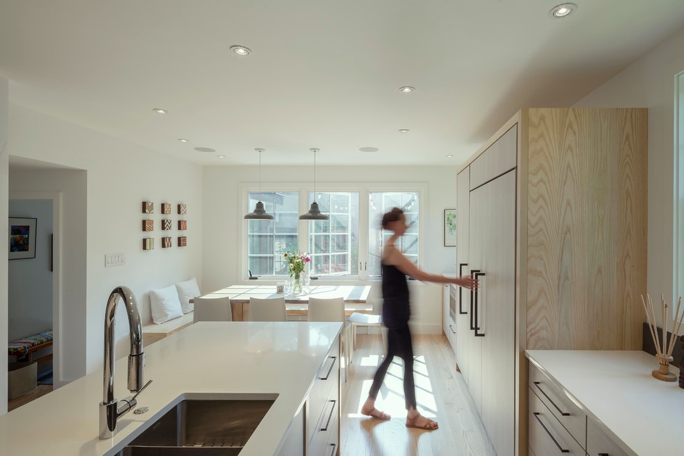Design ideas for a contemporary galley kitchen/diner in Boston with a double-bowl sink, flat-panel cabinets, light wood cabinets, integrated appliances, light hardwood flooring, an island, black splashback, metro tiled splashback and white worktops.