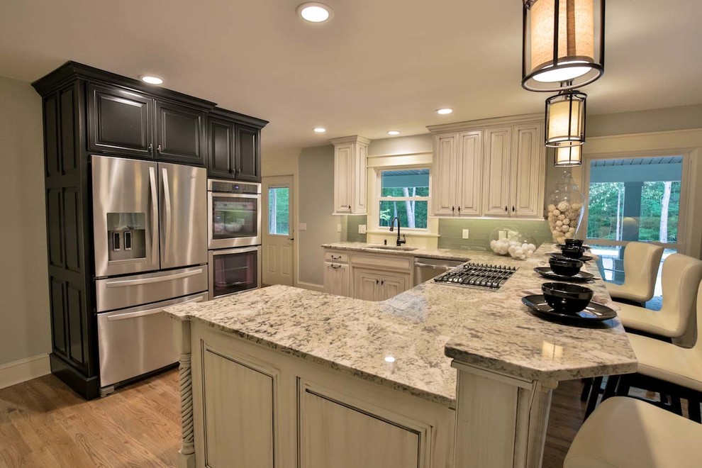 Example of a large trendy l-shaped light wood floor open concept kitchen design in Atlanta with an undermount sink, raised-panel cabinets, dark wood cabinets, granite countertops, green backsplash, glass tile backsplash, stainless steel appliances and a peninsula