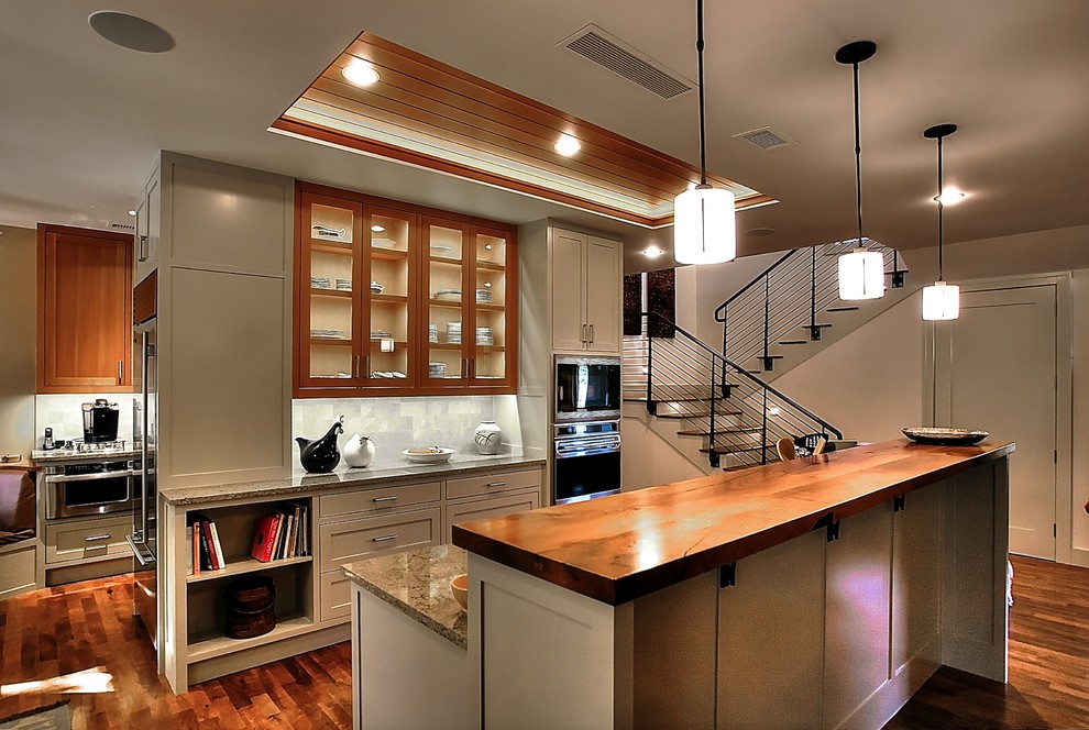 Imagen de cocina contemporánea grande abierta con armarios tipo vitrina, puertas de armario de madera clara, salpicadero beige y electrodomésticos de acero inoxidable