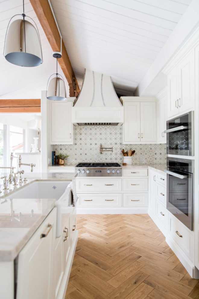Foto de cocina actual con armarios estilo shaker, puertas de armario blancas, suelo de madera en tonos medios, una isla, suelo marrón y encimeras negras