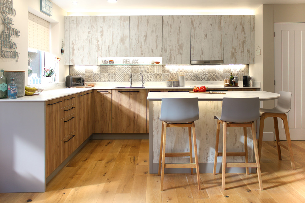 Foto på ett mellanstort funkis vit l-kök, med en undermonterad diskho, släta luckor, skåp i slitet trä, laminatbänkskiva, grått stänkskydd, stänkskydd i porslinskakel, mellanmörkt trägolv, en köksö och brunt golv