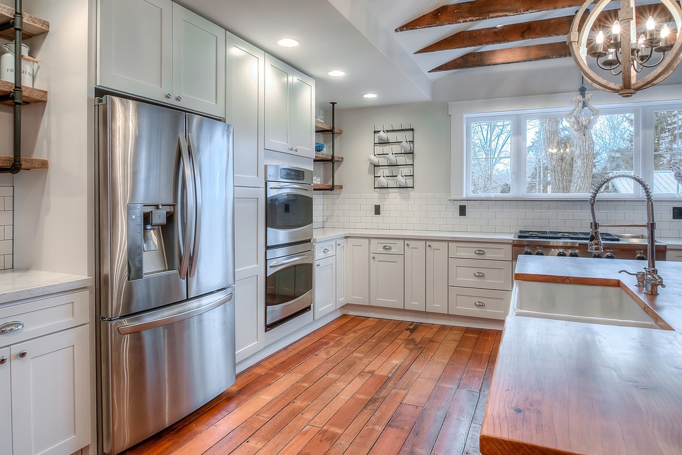 Bild på ett mellanstort lantligt kök och matrum, med en rustik diskho, vita skåp, träbänkskiva, vitt stänkskydd, stänkskydd i keramik, rostfria vitvaror, mellanmörkt trägolv och en köksö
