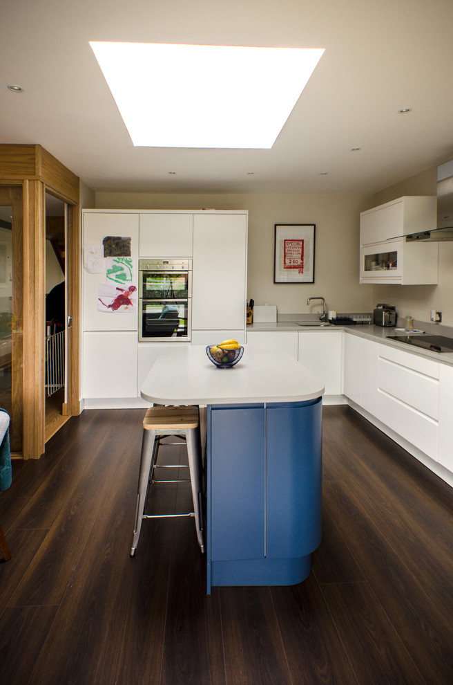 Moderne Küche mit weißen Schränken, Quarzit-Arbeitsplatte, weißen Elektrogeräten, Kücheninsel und braunem Boden in Dublin