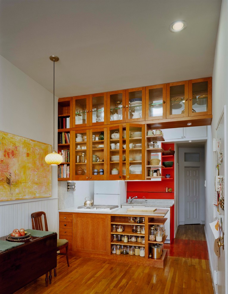 Ejemplo de cocina de tamaño medio abierta con armarios tipo vitrina, puertas de armario de madera clara, encimera de terrazo, salpicadero rojo, suelo de madera en tonos medios y península